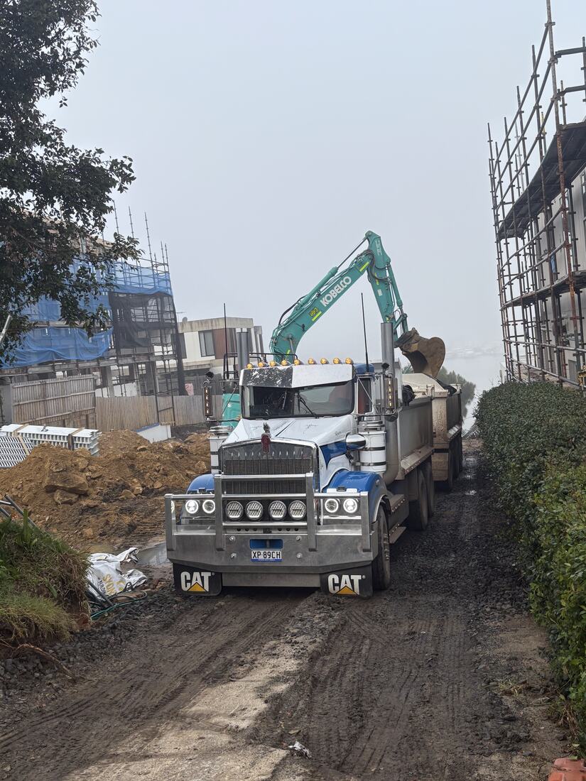 Excavator loading a Kenworth truck and dog at a build site